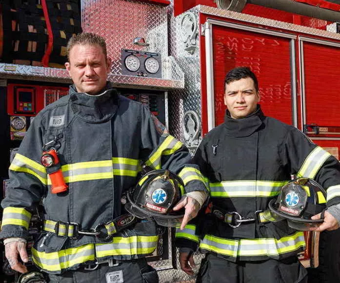 Two Firemen Standing Next to Firetruck